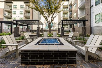 An outdoor patio with a firepit and chairs and an apartment building
